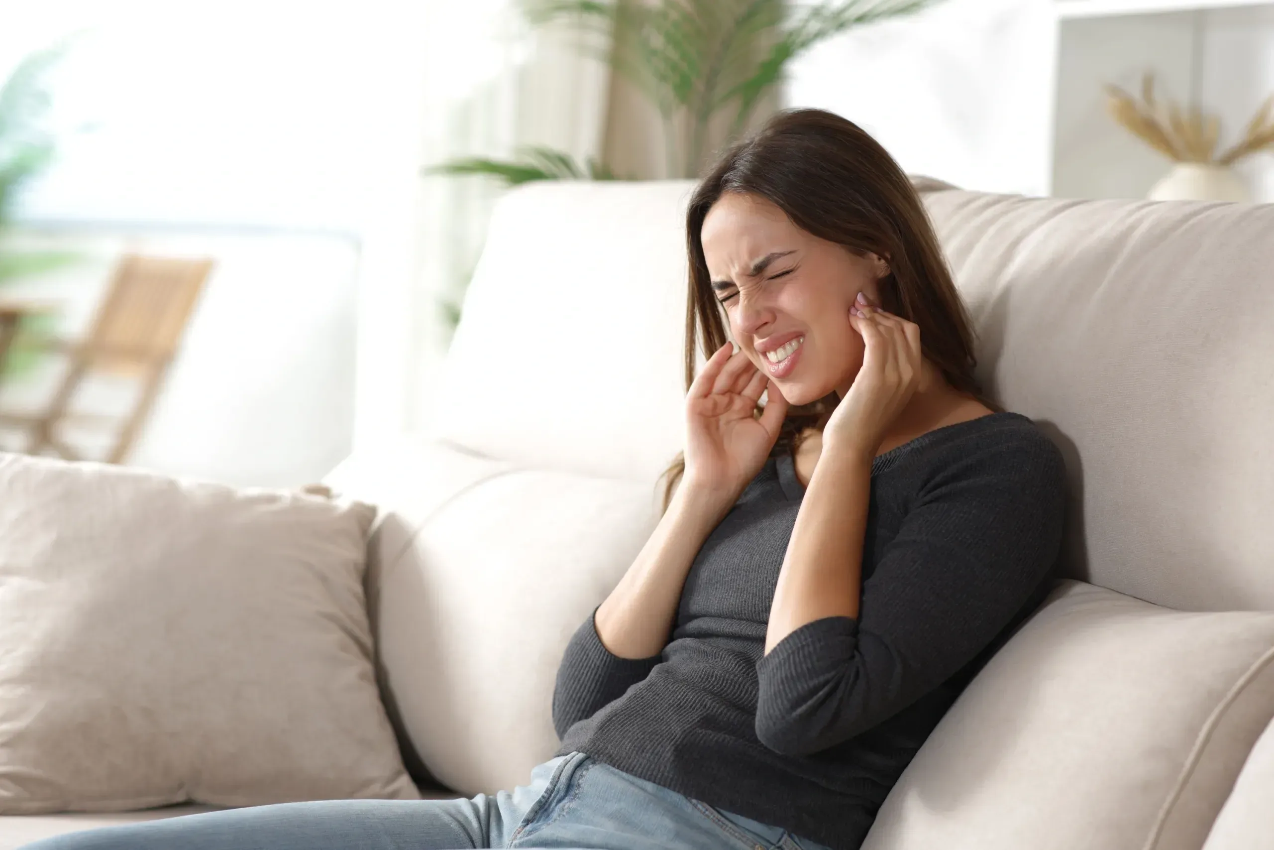 Woman pressing her fingertips to a sore jaw on waking, a common sign of nighttime clenching and TMJ strain