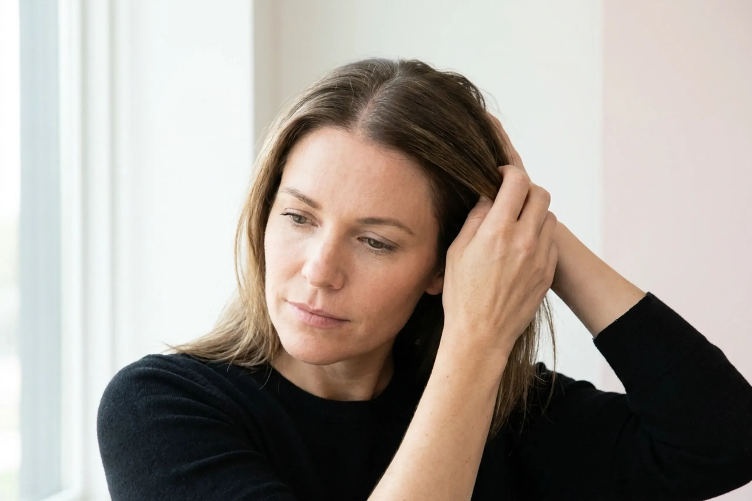 Woman parting her hair to reveal diffuse crown thinning before hair loss treatment in Covington, KY